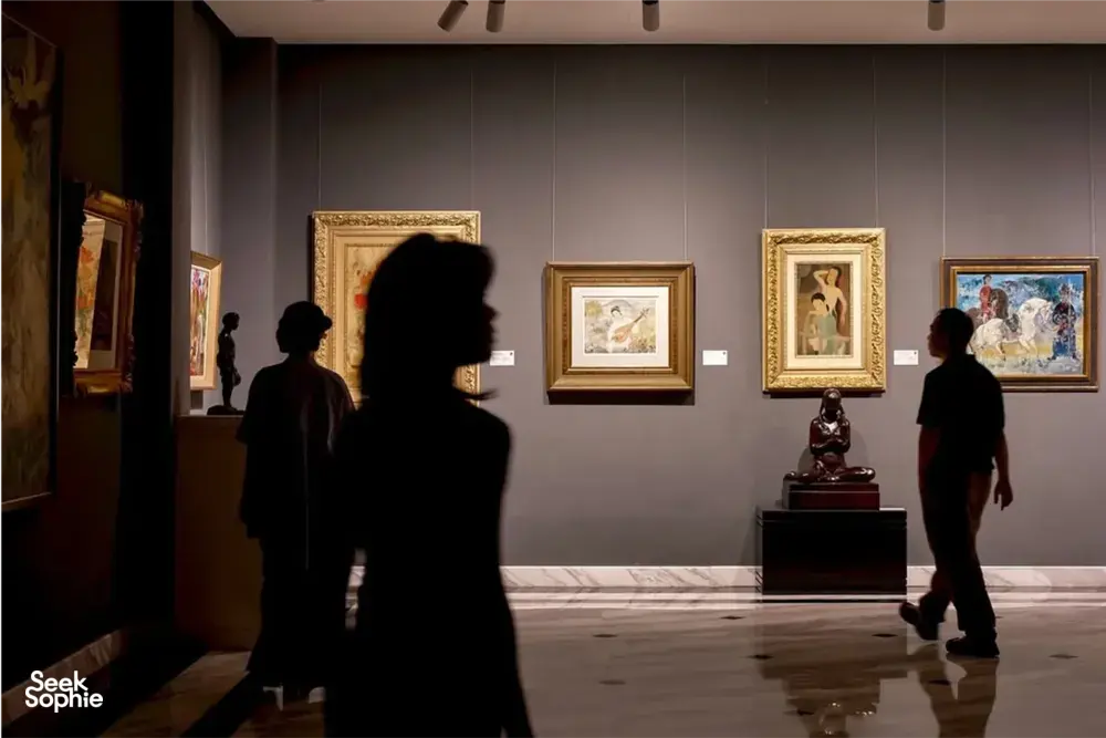 Silhouetted visitors stroll past framed artworks on an expert-led Vietnamese art tour at Quang San Art Museum in Ho Chi Minh City