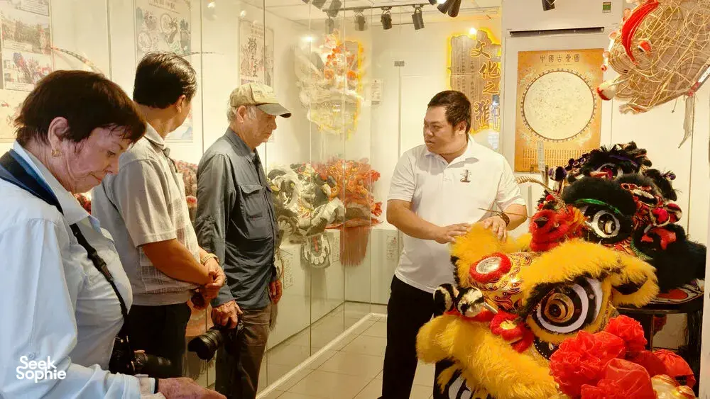 Visitors studying lion dance costumes and a dragon head in an indoor Ho Chi Minh City exhibit on kung fu traditions