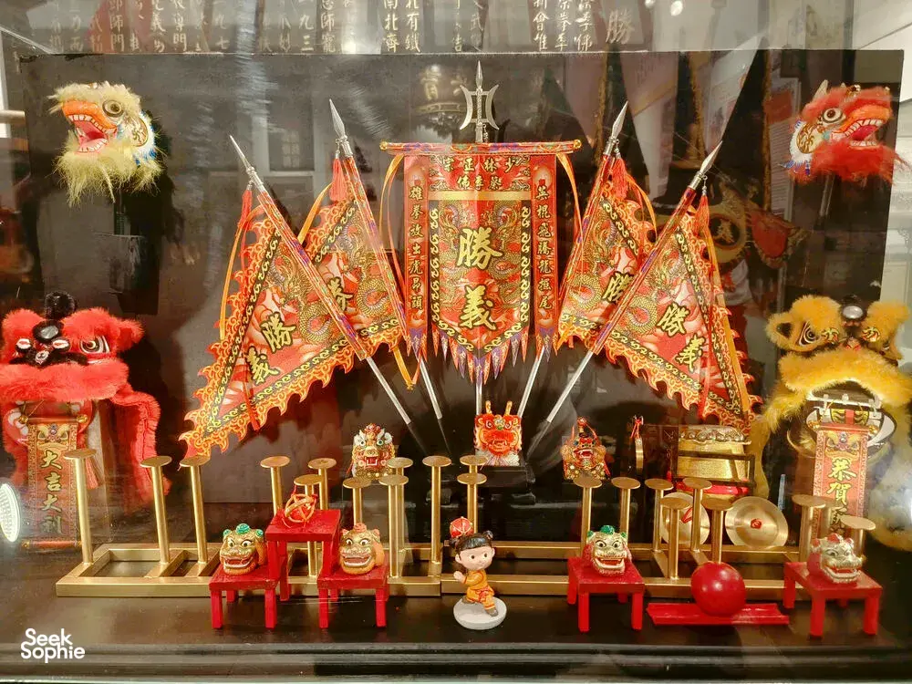 Lion dance headpieces, small guardian lion figures and an ornate red ceremonial banner displayed in a Ho Chi Minh City kung fu room