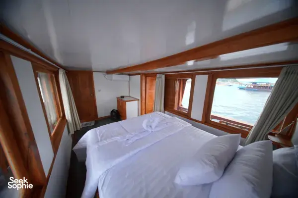 Cozy wooden boat cabin with a made double bed and wide windows looking out to the harbour water in Labuan Bajo
