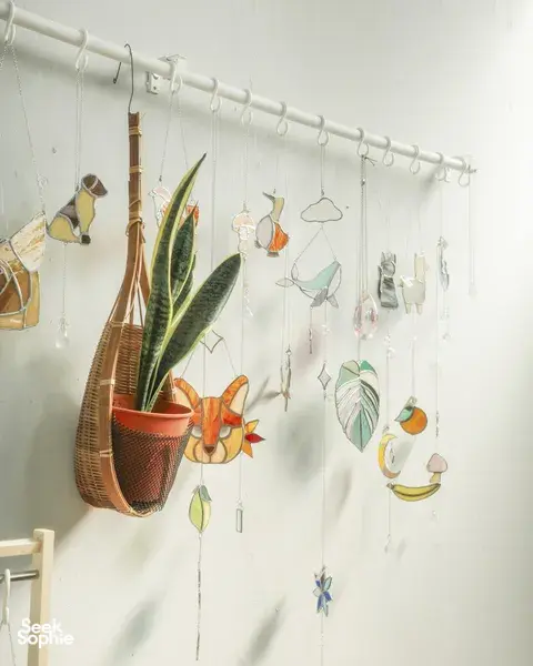 Hanging stained-glass suncatchers shaped like birds and leaves on a display rail in a bright studio at craft workshops in Singapore