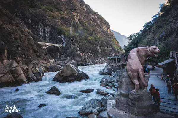 Rocky river gorge in China with fast-flowing water, a riverside walkway, and a large stone animal statue