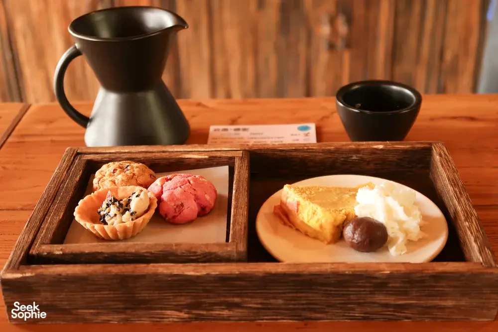 Coffee cupping tray with pastries and black cups beside a small coffee pot at the family-run specialty coffee workshop in Lijiang