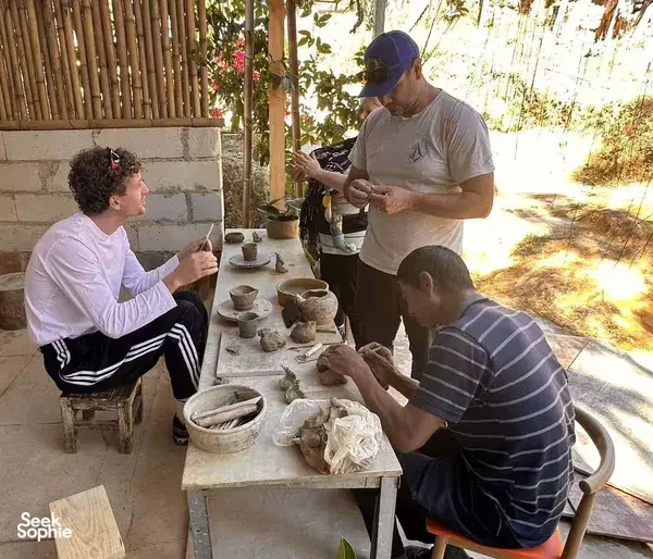 Visitors seated at a pottery table in Shangri-La, shaping and glazing small clay cups during a guided village workshop
