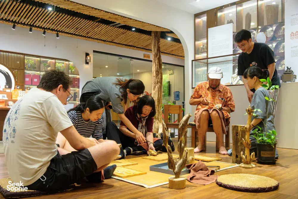 Guests kneel around a table of agarwood samples during a guided Hanoi workshop in a bright exhibition space