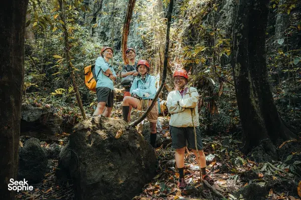 Hikers pause on a forest trail among tall trees and boulders during a Phong Nha cave trekking adventure