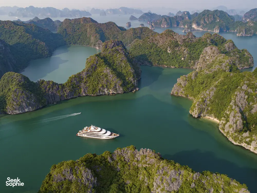 Aerial view of limestone karst islands and a cruise ship gliding through turquoise waters in Halong Bay