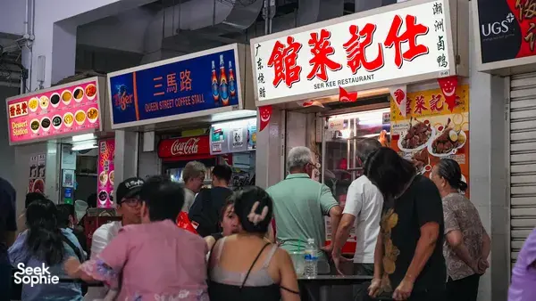 Busier Singapore hawker centre lane with diners queuing in front of street-food stalls under colourful signage — Singapore hidden gems