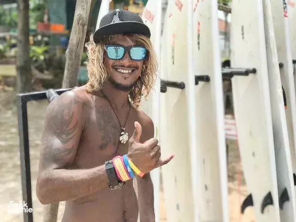 Freedom Surf Sri Lanka instructor grinning and giving a thumbs-up in Weligama beside upright surfboards at the surf camp