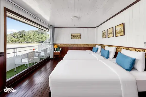 Halong Bay party cruise cabin with a double bed, blue cushions, and large windows showing the lake view outside
