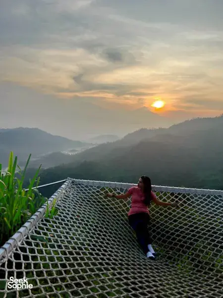 Sitting on a netted lookout platform watching sunrise over hazy valley and volcano ridges in Yogyakarta on Picnic Indonesia coffee farm tour