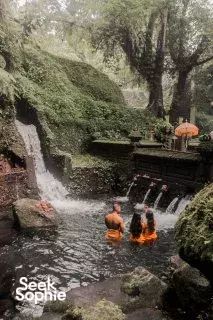 People relaxing in a natural rock pool with a waterfall in Indonesia during a yoga retreat, seated and soaking in warm water