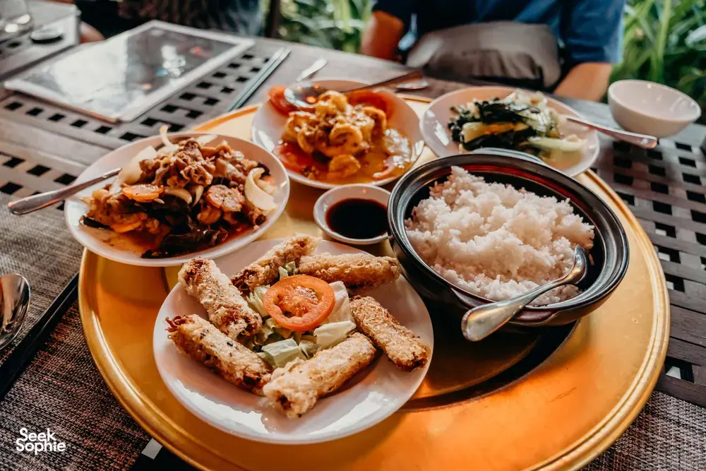 会安美食之旅的餐食摆放在编织桌面上:白盘里有一碗米饭、炸开胃小食和炒菜