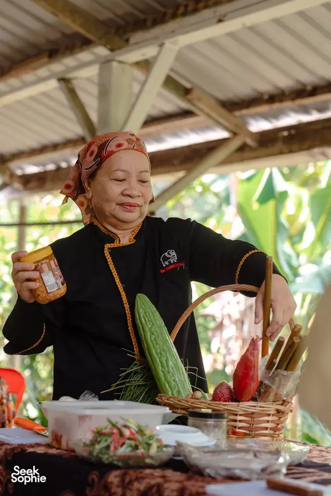 Indigenous Sabahan family cook holding a spice jar at a wooden table outdoors in Kota Kinabalu, Sabah