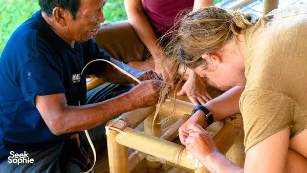 Traditional Balinese bamboo craftsmen and a participant binding bamboo joints inside a Bali construction workshop, hands at work