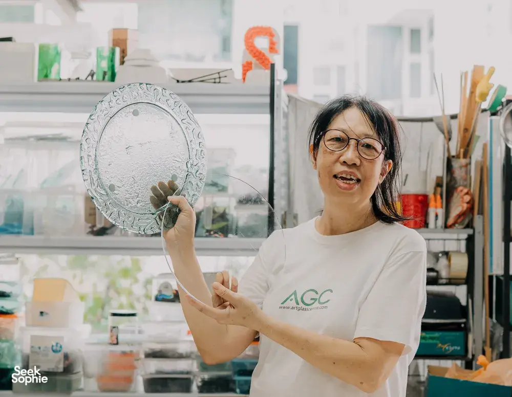Tan Sock Fong holding a textured round glass piece at Art Glass Centre in Singapore, showing centrepiece skills—workshops in Singapore