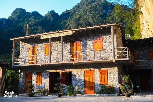 Stone-and-wood homestay building with orange doors and shutters in Cao Bang, set against rocky hills on the loop