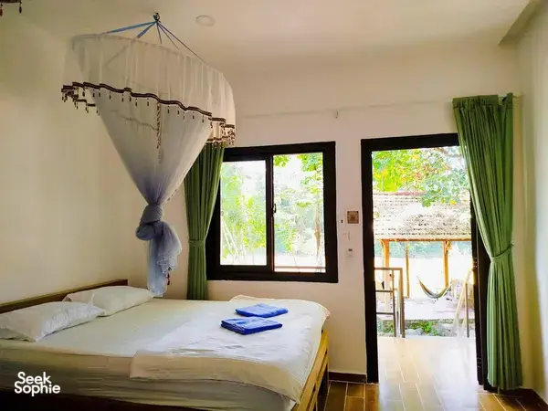 Green Hope Lodge room with four-poster canopy bed, green curtains, and terrace view of trees at Cat Tien, 2D1N stay