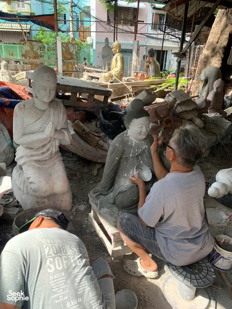 Saigon sculpture workshop where artisans work on white clay statues, with plaster figures and tools arranged along a sunlit aisle