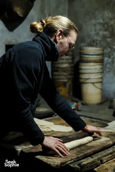 Person flattening and cutting dough on a wooden workbench inside a Hoi An workshop on an early-morning trades ride