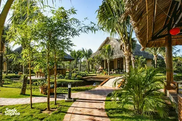Garden path beside thatched villas at The Island Lodge, a luxurious Mekong Delta resort with palms and manicured lawns