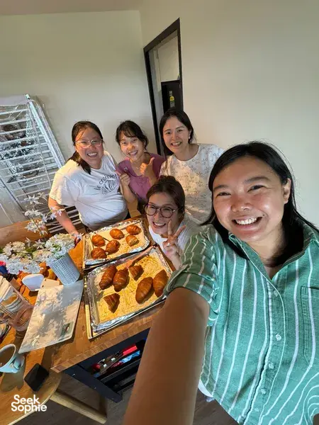 Smiling group beside a baking table of freshly baked pastries and trays in a kitchen during The Daily Staples workshops in Singapore