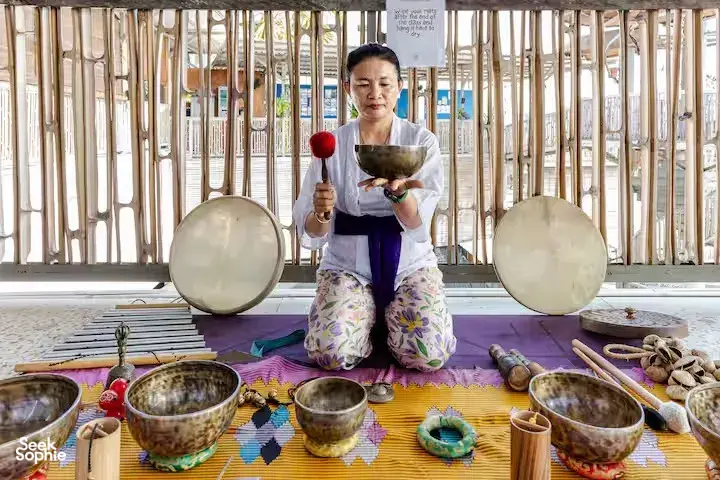 ADDA Yoga sound healer seated with singing bowls on a rooftop mat in Canggu, Bali for a sound healing session