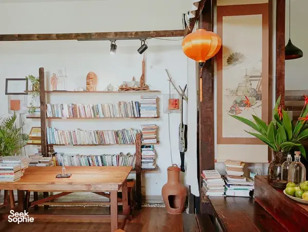 Sudut tenang di Chan Dat Living Room di Hoi An, dengan rak buku kayu, meja belajar, dan lentera oranye yang bercahaya