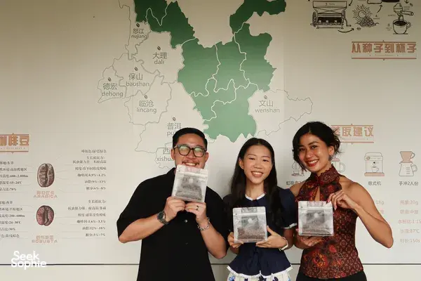 Tasting participants hold up Yunnan coffee sample bags in front of a map wall during a specialty workshop in Lijiang