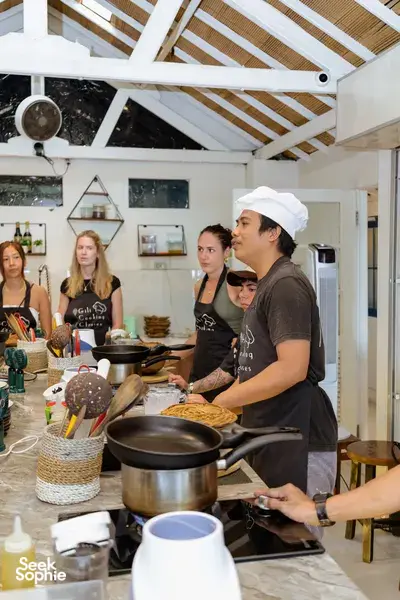 Chef leading an Indonesian cooking class on Gili T in Lombok, stirring in a pan as guests watch from the counter