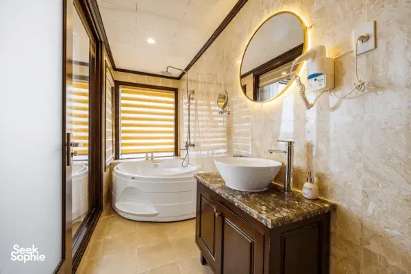En-suite bathroom on the Oasis Bay Party Cruiser with a round bathtub, stone-tiled vanity and mirror lighting in Halong Bay