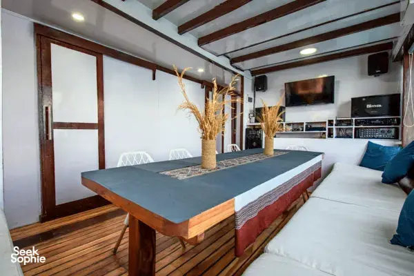 Dining table and sofa seating inside a sleek phinisi cabin on La Famille’s private 3D2N Komodo cruise in Labuan Bajo