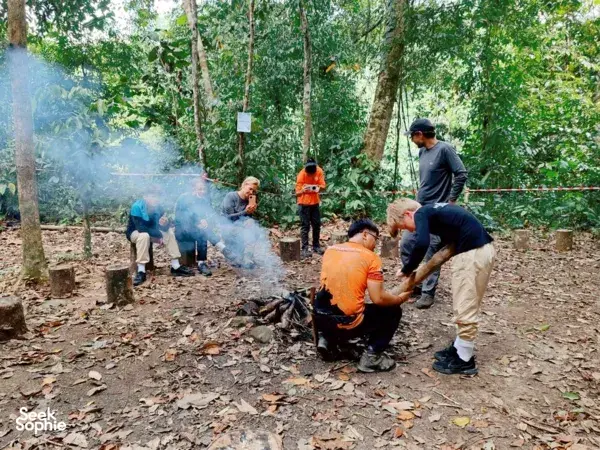 Outreach Borneo group gathered around a campfire in the forest, with smoke from cooking during a jungle adventure near Kota Kinabalu