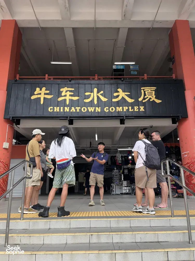 旅客在新加坡牛车水大厦入口招牌旁等候,准备参加粤语鱼市之旅与小贩中心步行体验