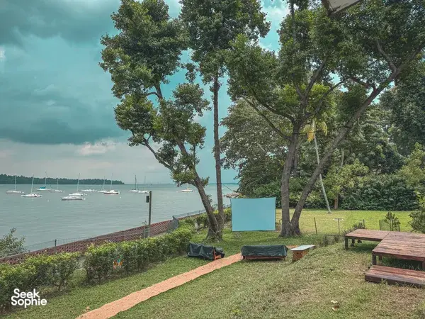 Garden lawn with wooden seating overlooking sailboats and calm harbour water at a Singapore farmstay by the sea, Singapore hidden gems