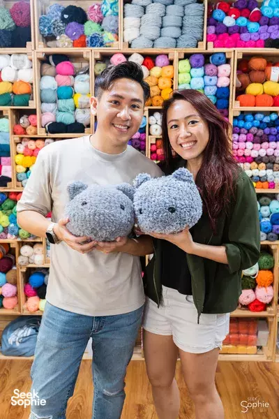 Two participants smiling while holding handmade blue plush toys in Tiny Rabbit Hole’s plush-filled studio in Singapore for workshops in Singapore