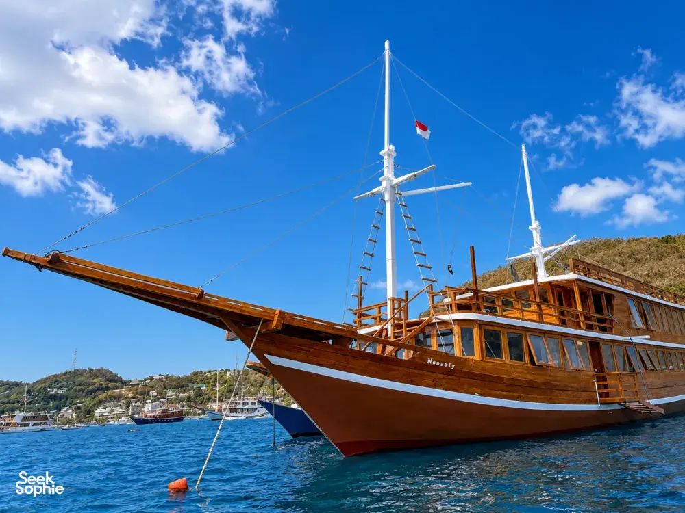 Newest wooden phinisi with raised masts and Indonesian flag cruising across blue water off Labuan Bajo