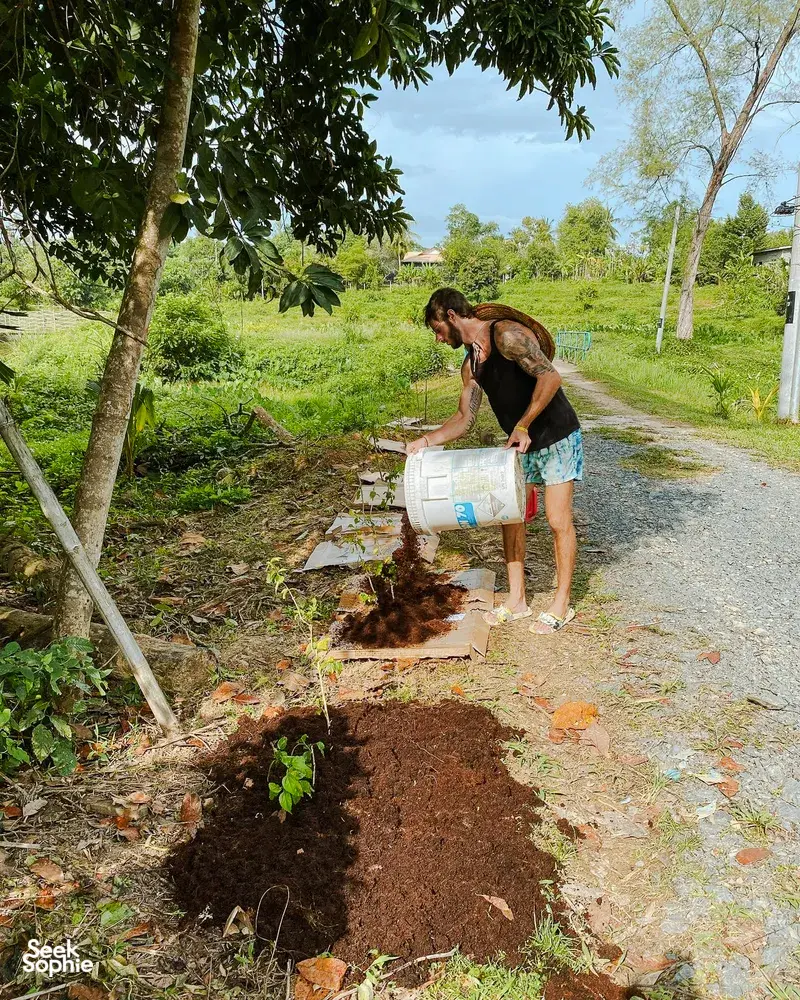 Gardener digging a new plot and filling it with soil at a Langkawi permaculture farmhouse, with a sack and tools
