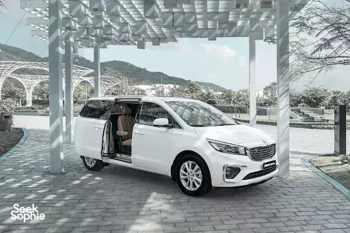 White people-carrier van parked beneath a modern canopy with mountains in the distance at a transport stop, Ho Chi Minh City