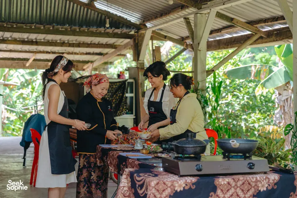 Local family and guests cooking and tasting near a bubbling pot on an outdoor table at an Indigenous Sabahan experience in Kota Kinabalu