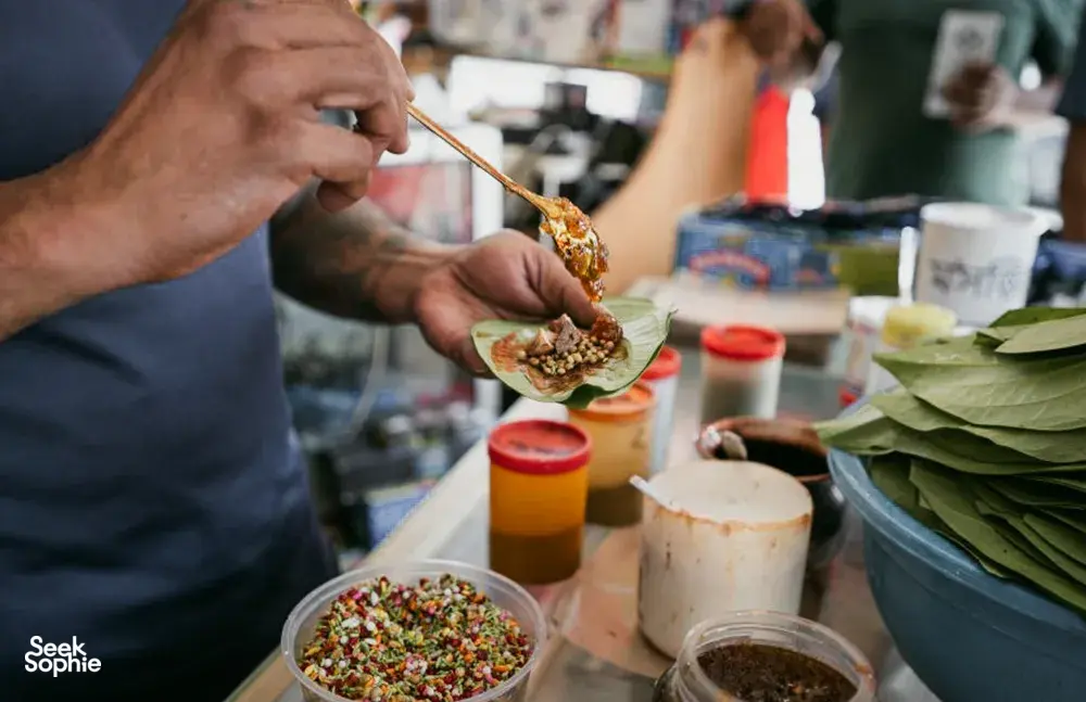 Tangan menyajikan hidangan pembuka ke piring beralas daun di atas meja, dari Hidden Heritage dalam pengalaman hidden gems Secrets of the Streets di Singapura