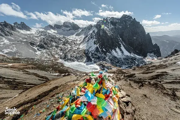Colourful prayer flags on a rocky pass overlooking snowy peaks in Shangri-La, surrounded by rugged hiking terrain