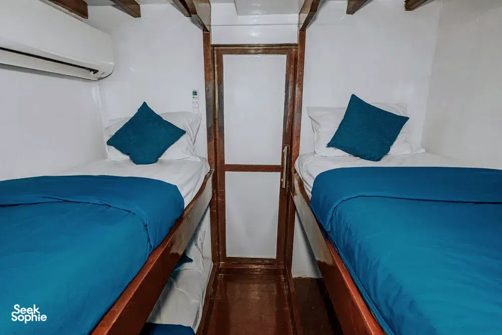 Narrow hallway between two twin bunks inside a phinisi cabin on a private 3D2N Komodo cruise, warm light at the doorway, Labuan Bajo