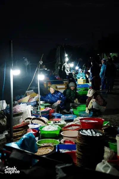 Vendors preparing food and supplies at a night-time market during a dawn Hoi An motorbike trades tour