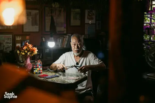 Seorang pria membungkuk di atas meja berisi kertas dan alat di bawah lampu gantung, untuk kisah sewa apartemen Hidden Heritage, permata tersembunyi Singapura
