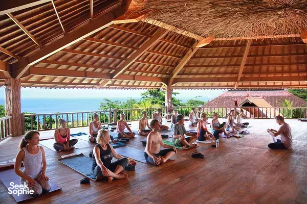 Yoga participants seated on mats inside an open-air pavilion with sea view at Udara Yoga retreat in Bali