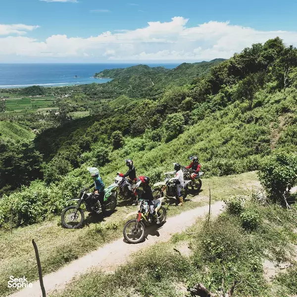 Group of dirt bikes on a winding track during a Lombok motorcycle tour, with riders overlooking farmland and the blue sea