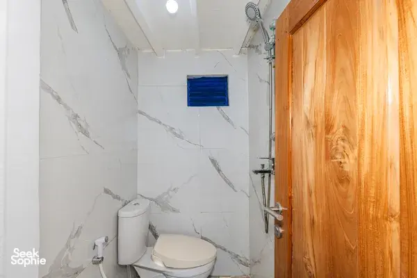 Bathroom on a Komodo liveaboard in Labuan Bajo, with marble-style walls, toilet, and hand shower at the sink