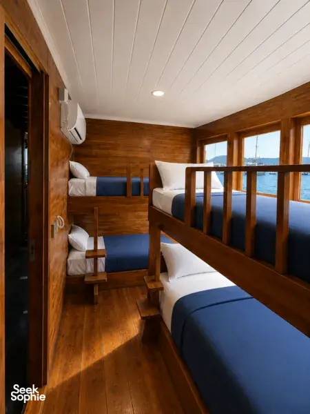 Wooden phinisi cabin with three berths and sea-view windows, with an air-conditioning unit on a shared Komodo cruise from Labuan Bajo