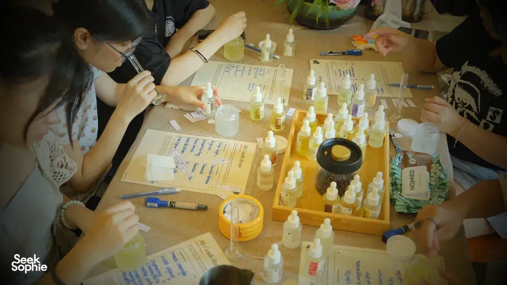 People at a shared bench in Singapore working with fragrance bottles and dropper tools during a coco-soy candle workshop